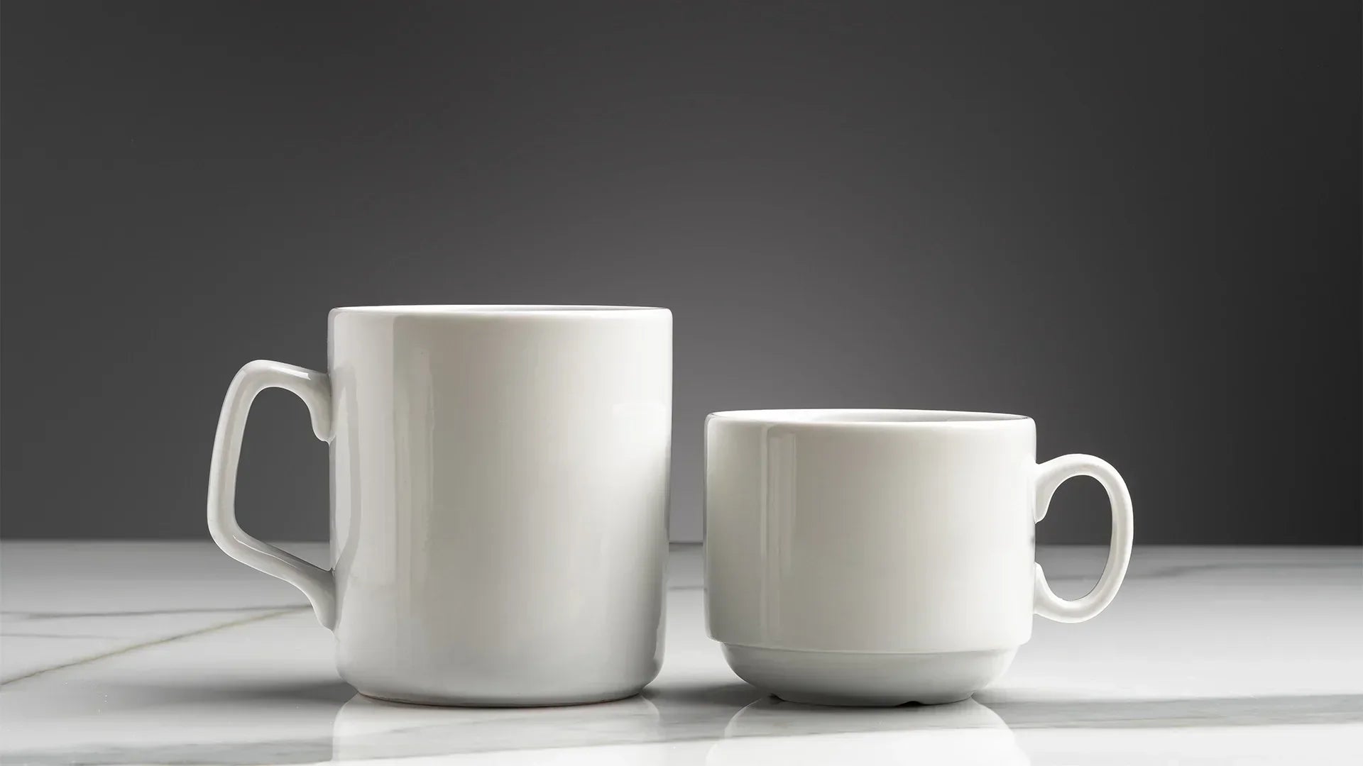 A white ceramic coffee mug and a white ceramic tea mug next to each other on a white table and grey background