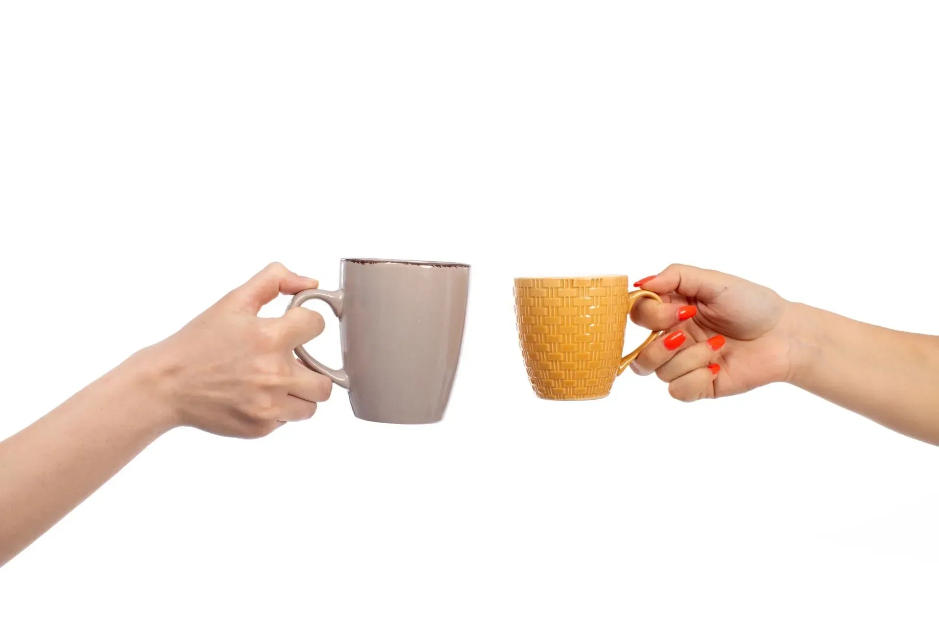 Two hands holding a mug and a cup facing each other on a white background.